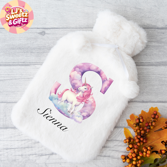 White hot water bottle with unicorn design and 'Sienna' text on a wooden surface with fall leaves.